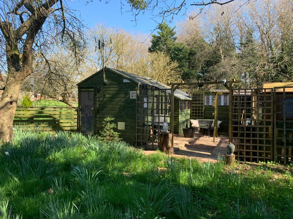 a green greenhouse in a garden with a fence at Hedgehog Lodge in Colwall