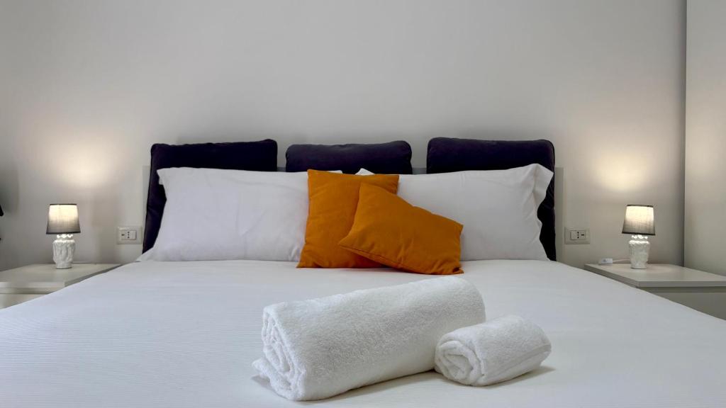 ein weißes Bett mit orangefarbenen und weißen Kissen darauf in der Unterkunft Sciara Marina, Fiumefreddo di Sicilia, NUOVA STRUTTURA in Fiumefreddo di Sicilia