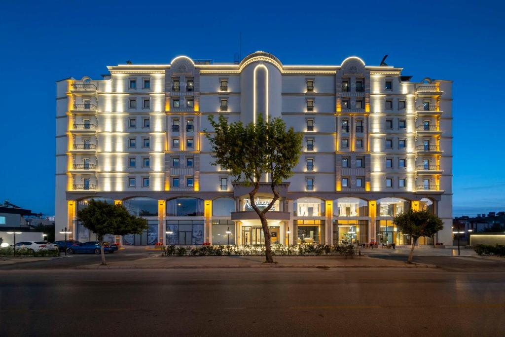 ein großes weißes Gebäude mit einem Baum davor in der Unterkunft Radisson Hotel Mersin in Mersin