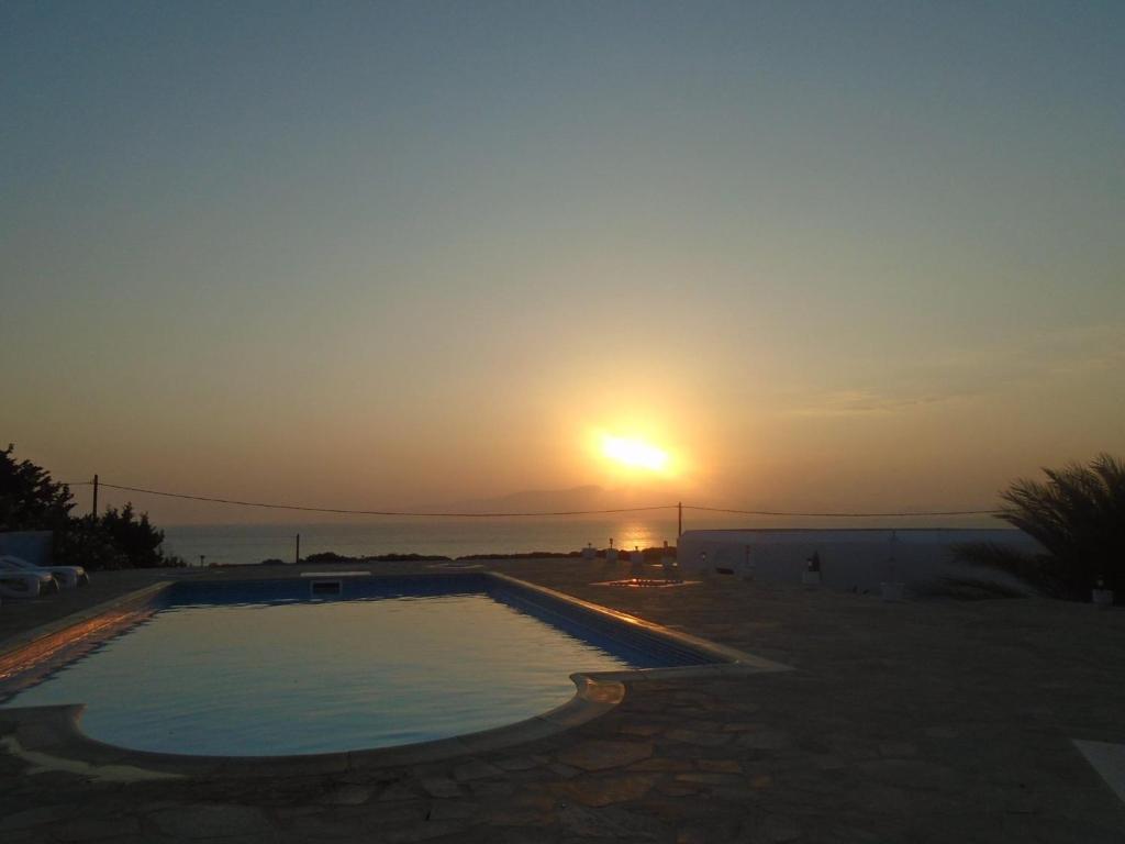 a sunset over a swimming pool with the sun in the sky at Portobello Naxos in Aliko Beach