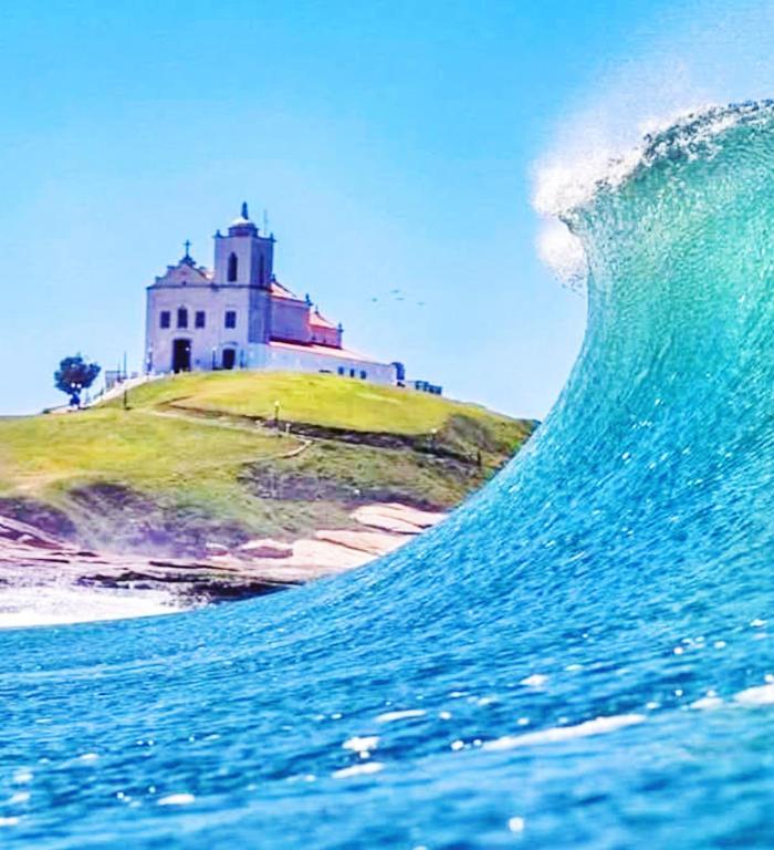 a wave in the ocean with a lighthouse in the background at Cobertura Pôr do Sol in Saquarema