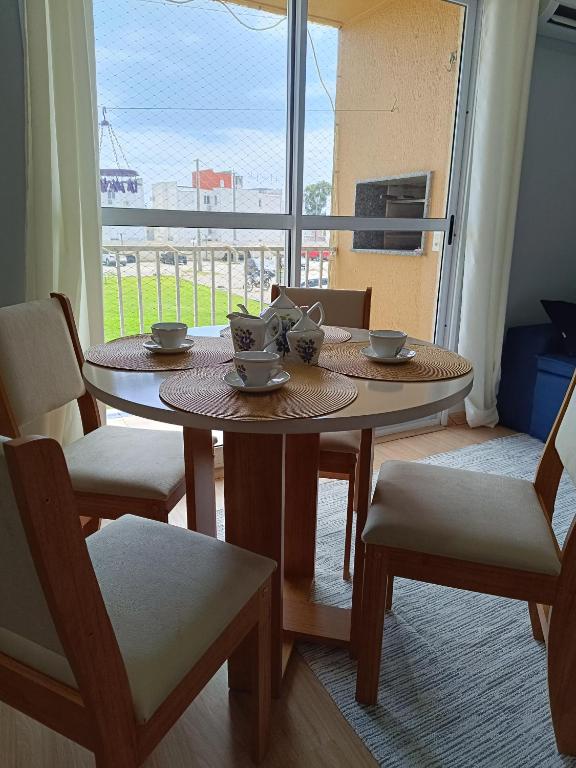a table with two cups and chairs and a window at Apartamento Umuharama in Pelotas