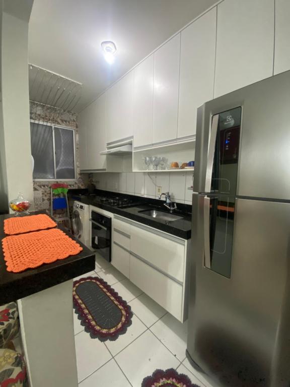 a kitchen with white cabinets and a stainless steel refrigerator at Apartamento com AR Condicionado splint, condomínio com piscina 2 Qts, próximo à praias e ao pavilhão de Carapina com portaria 24h in Serra