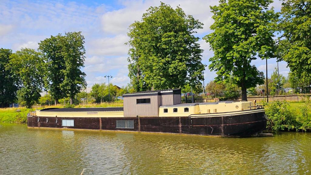un bateau avec un bâtiment au bord d'une rivière dans l'établissement La Péniche - Gîte de groupe insolite, à Saint-Omer