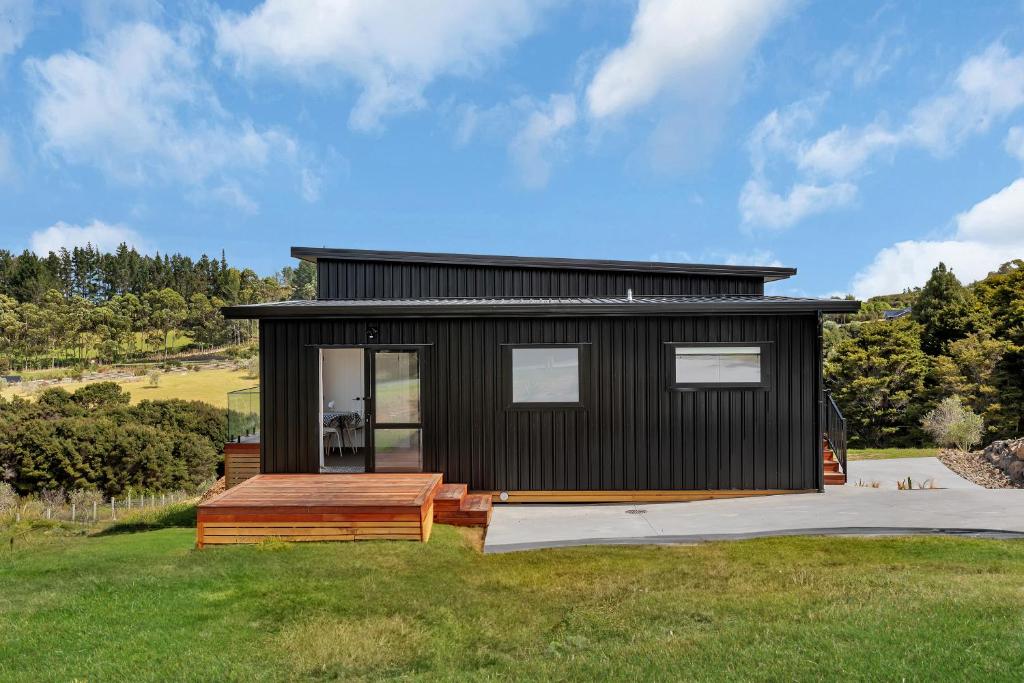 a black tiny house with a wooden deck at Central Couples Retreat - Mangawhai Heads Unit in Mangawhai