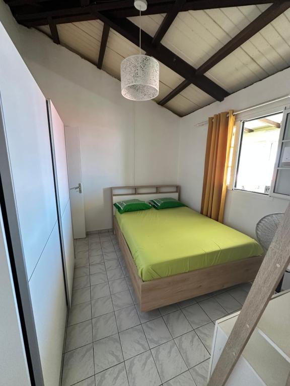 Un dormitorio con una cama verde y una ventana. en Jolie maison saisonnière en Guadeloupe de 160m2 disposant de 4 chambres 2 toilettes une grande véranda et terrasse, en Vieux-Fort