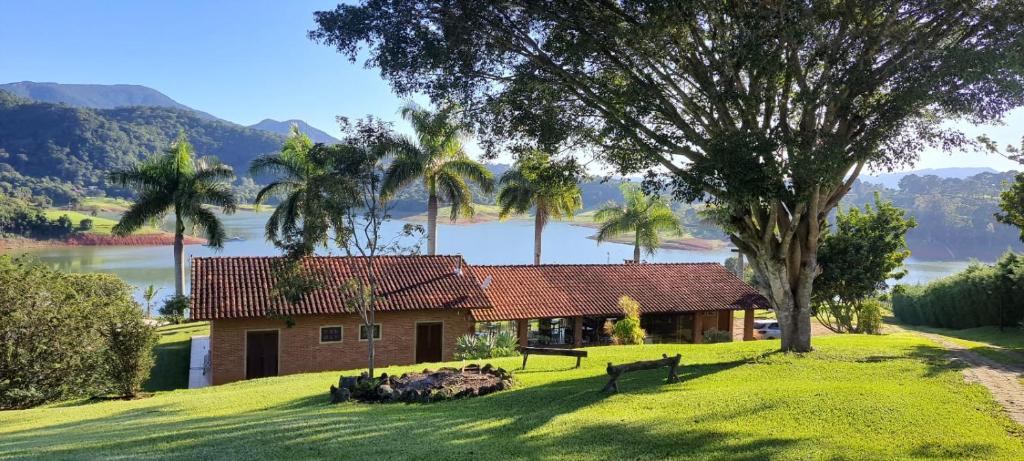 ein Haus auf einem Hügel mit einem Baum und einem See in der Unterkunft Chalé Represa Varanda do Sol - Chalé Alvenaria in Joanópolis
