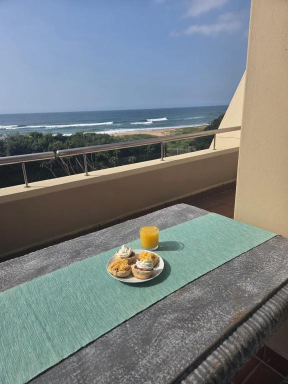 a table with a plate of food and a glass of orange juice at Ocean View Family Apartment - L'Escalier 208 a ABR3 Haven in Amanzimtoti