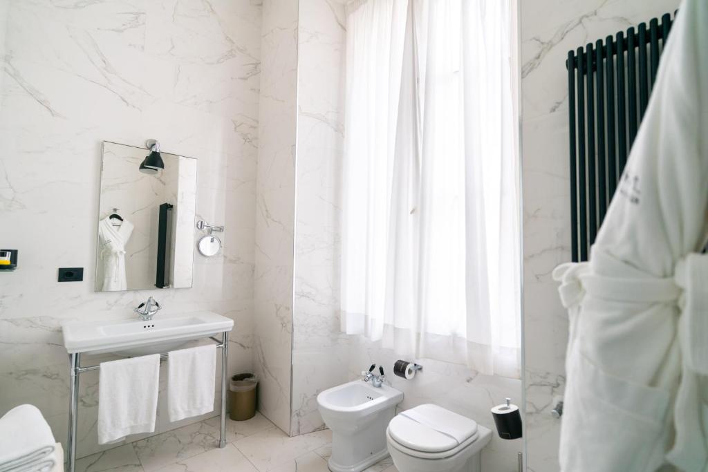 a white bathroom with a toilet and a sink at Roma Luxus Hotel in Rome