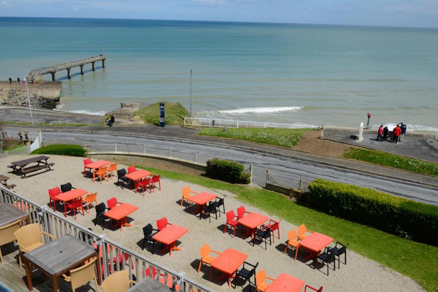 a group of tables and chairs next to the beach at Logis Hotel Du Casino Restaurant Le Mathelia in Vierville-sur-Mer