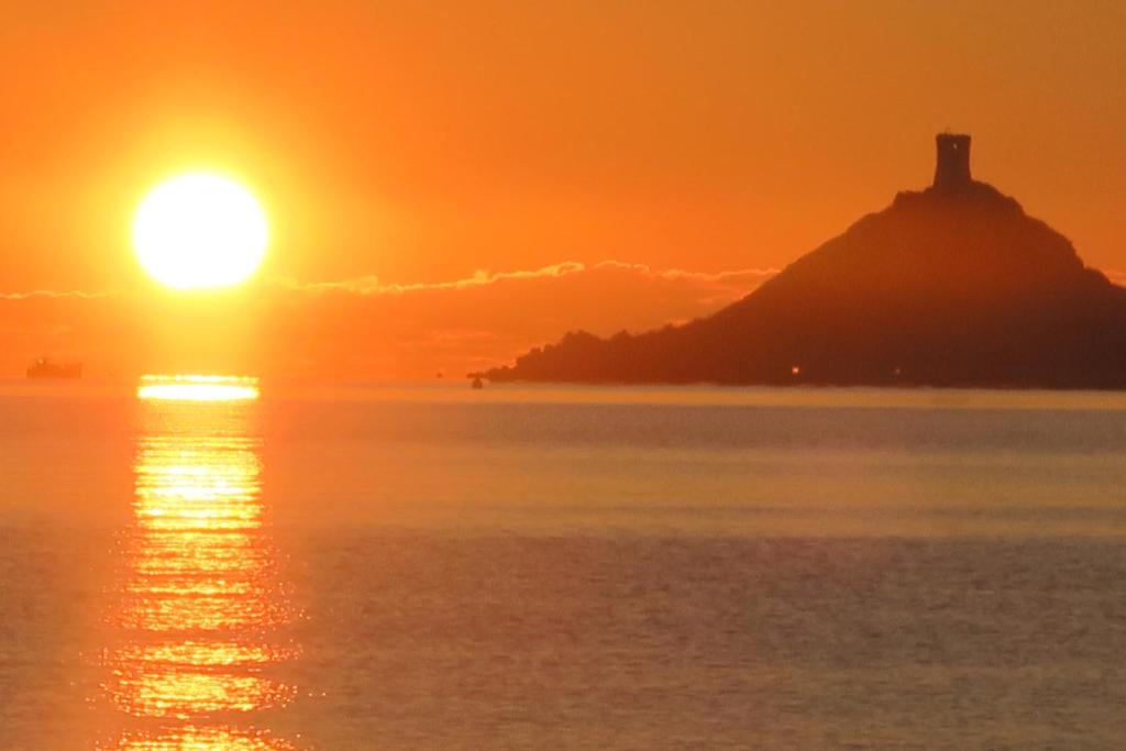un coucher de soleil sur l'océan avec un phare sur une île dans l'établissement STUDIO LES CALANQUES, à Ajaccio