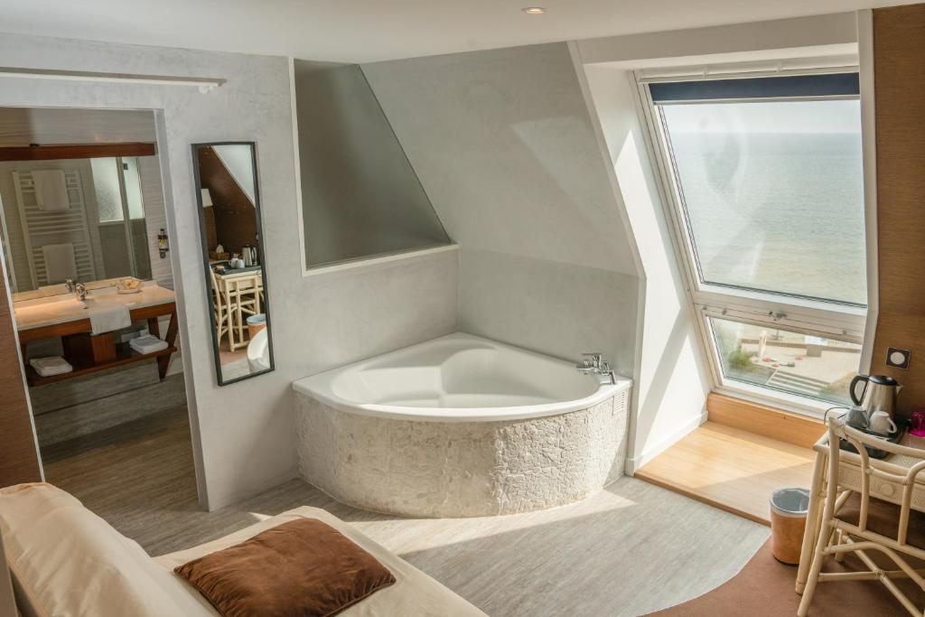 a large bath tub in a bathroom with a window at Logis Hotel Du Casino Restaurant Le Mathelia in Vierville-sur-Mer