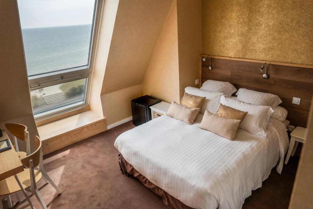 a bedroom with a bed and a large window at Logis Hotel Du Casino Restaurant Le Mathelia in Vierville-sur-Mer