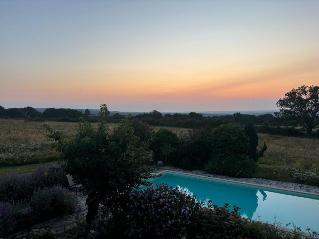 une piscine dans un jardin avec un coucher de soleil en arrière-plan dans l'établissement Bruyère en Fleur, à Clugnat