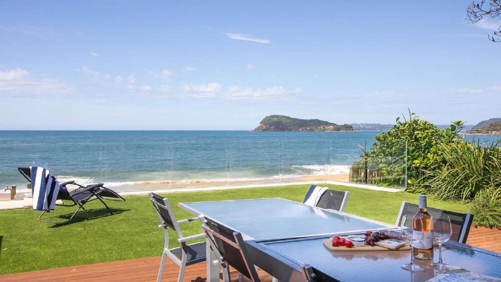 a blue table and chairs on a deck with the ocean at The Bach Pearl Beach-Absolute Beachfront , Late Check Out in Pearl Beach