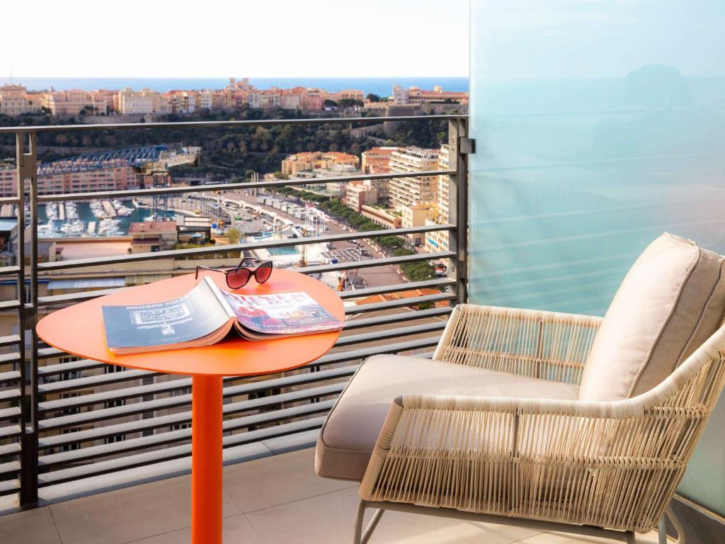 a table with a book and chairs on a balcony at Novotel Monte-Carlo in Monte Carlo