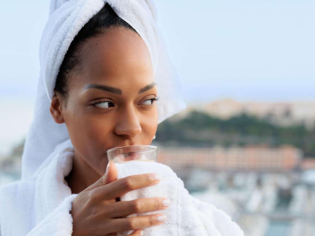 a woman in a towel drinking a glass of milk at Novotel Monte-Carlo in Monte Carlo