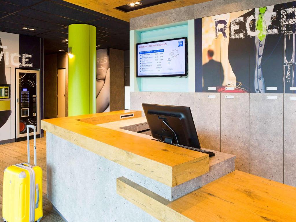 a lobby with a desk with a computer and a suitcase at ibis budget Montceau les Mines in Montceau-les-Mines
