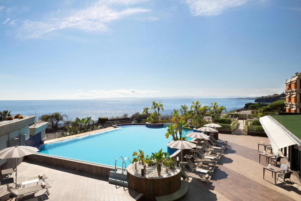 une image d'une piscine avec des chaises et des parasols dans l'établissement Four Points by Sheraton Catania Hotel, à Catane