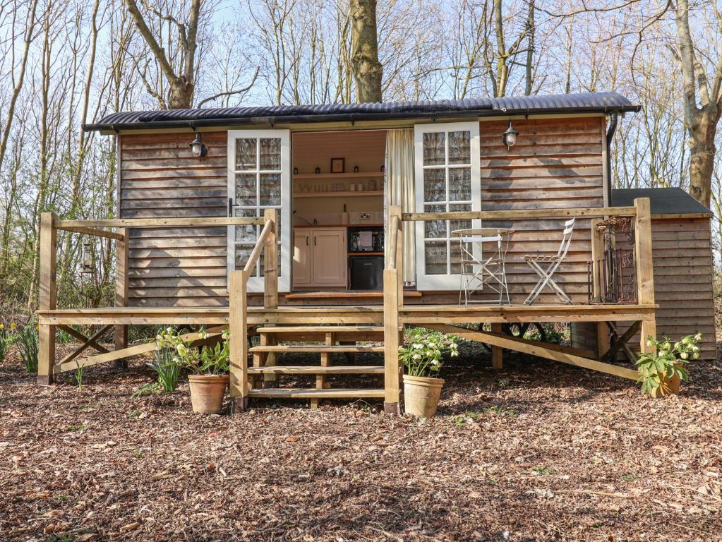 Una pequeña casa en el bosque con un porche. en Woodlands Retreat Shepherd's Hut, en Woodbridge