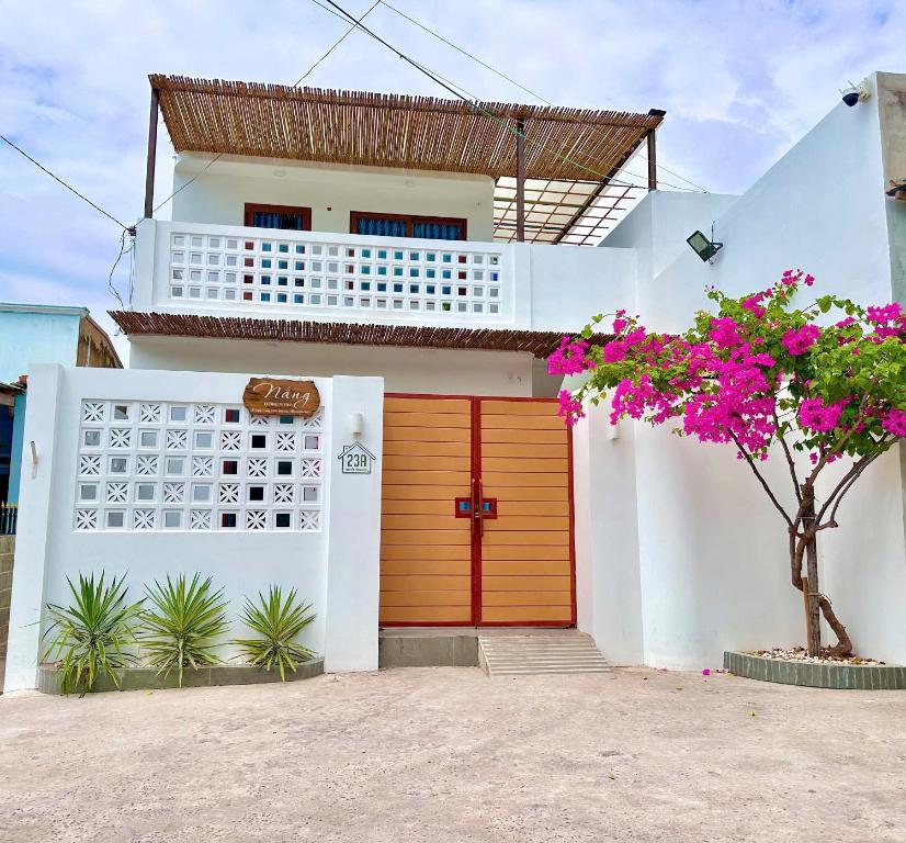 a white house with a orange door and a tree at NẮNG Homestay - Làng Chài Mũi Né - Mui Ne Fishing Village in Mui Ne