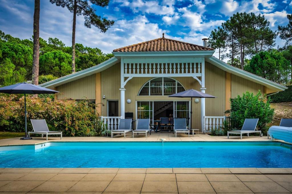 une maison avec une piscine, des chaises et des parasols dans l'établissement Villa élégante à Lacanau + piscine, à Lacanau