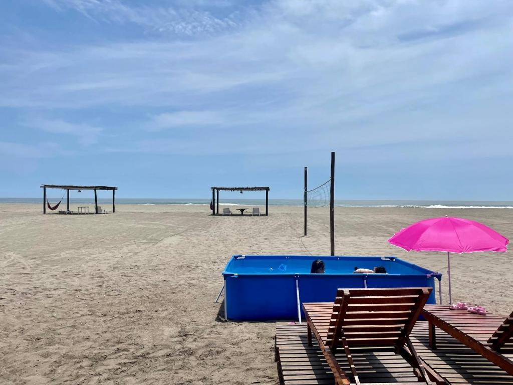 a beach with two chairs and an umbrella and two swings at Casa de playa en Wakama in San Vicente de Cañete
