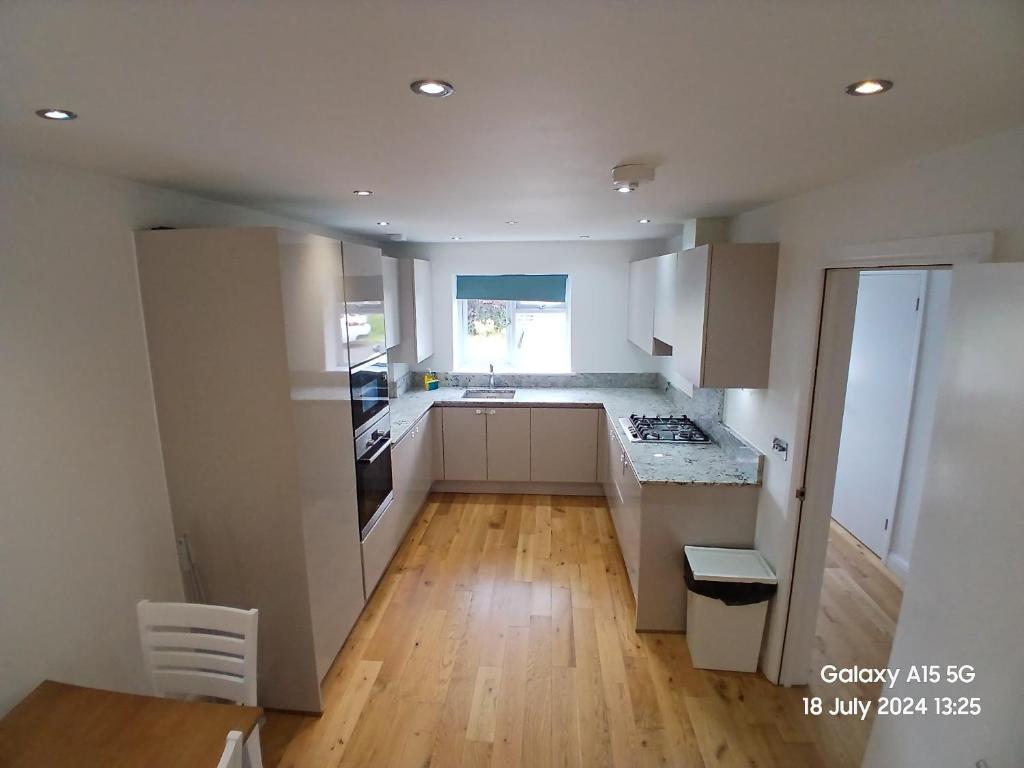 cocina con armarios blancos y suelo de madera en Hornchurch House - Romford, en Harold Wood
