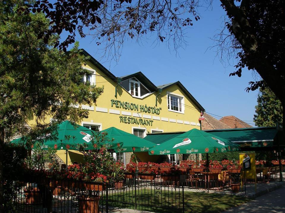 a yellow building with tables and green umbrellas at Pension Hostad in Gabčíkovo