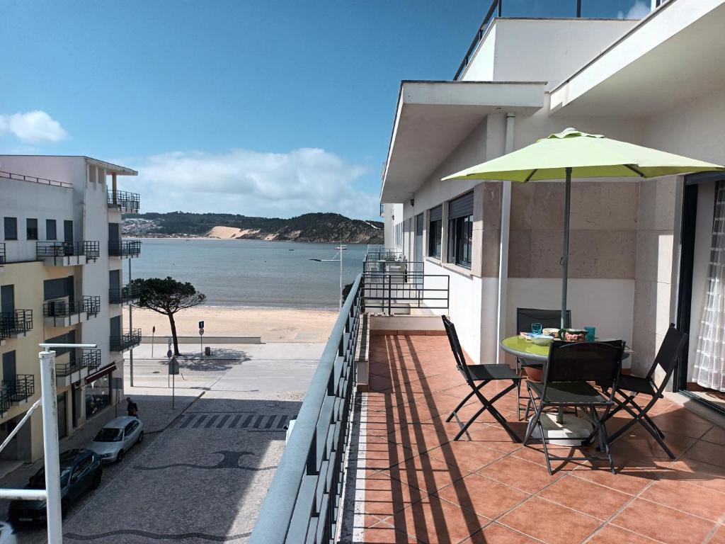 ein Balkon mit Tisch und Sonnenschirm und der Strand in der Unterkunft Terraço da Baía in São Martinho do Porto