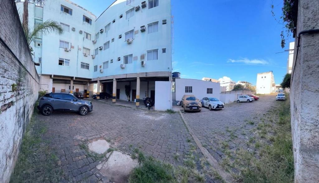 een groot wit gebouw met auto's geparkeerd op een parkeerplaats bij Hotel Hebron in Três Marias