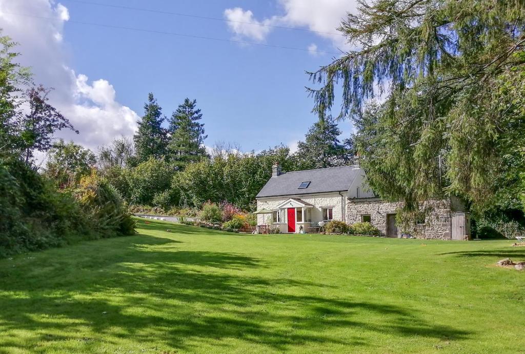 ein Steinhaus mit einer roten Tür auf einem Rasen in der Unterkunft Pwll Cottage in Carmarthen