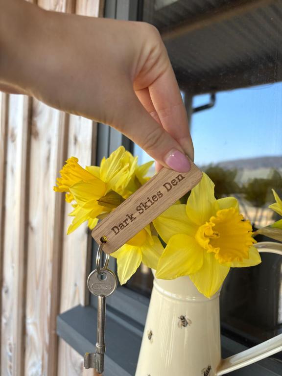 a hand holding a wooden key to a vase filled with flowers at Dark Skies den in Fryup