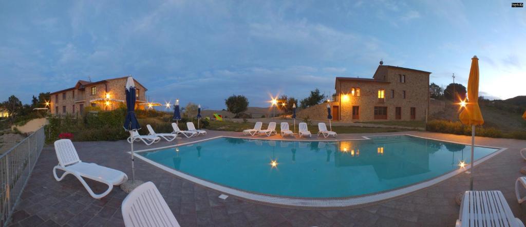 une piscine avec des chaises blanches et une maison dans l'établissement Agriturismo Il Noce, à Orciatico