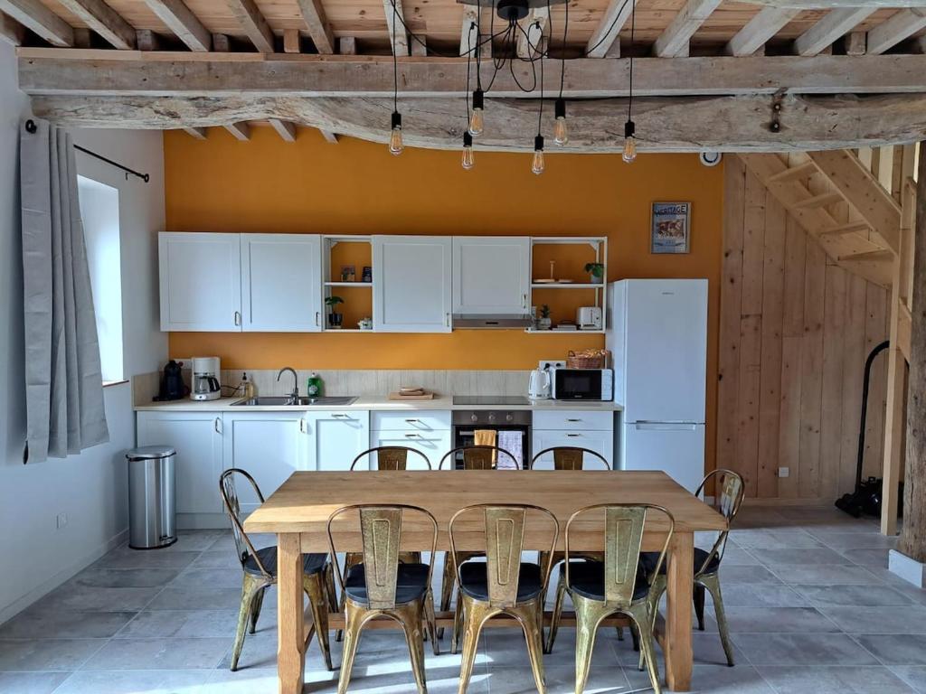 a kitchen with a wooden table with chairs and a refrigerator at Le Gîte Marguerite in Colleville