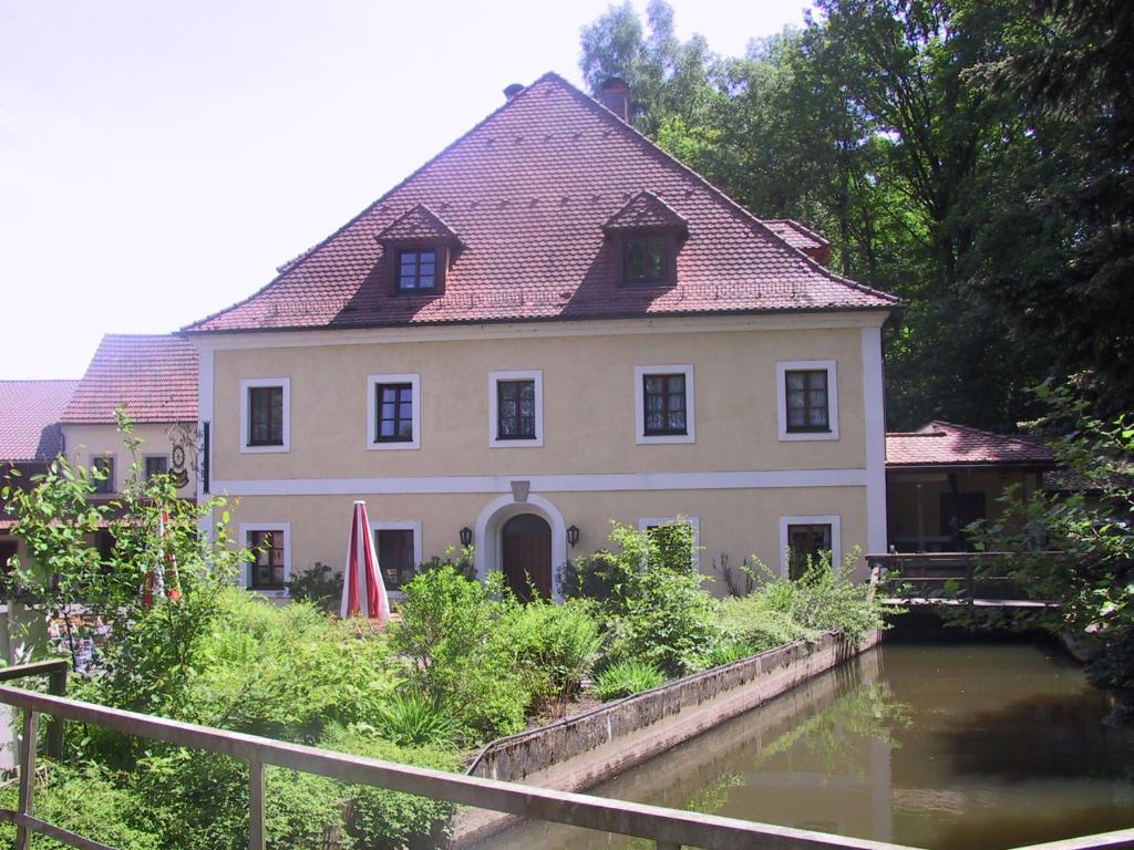 ein großes Haus mit einem Fluss davor in der Unterkunft Landhotel Kahrmühle in Pressath
