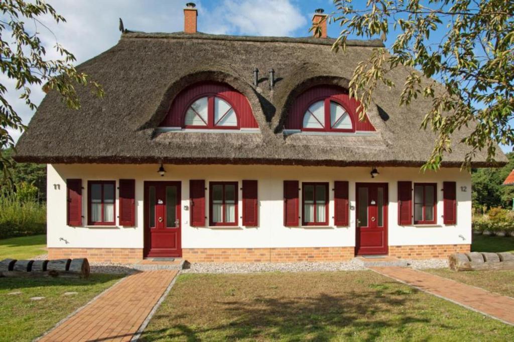 ein Haus mit einem Strohdach und roten Türen in der Unterkunft Dünenresidenz Glowe - Haus Lena in Glowe