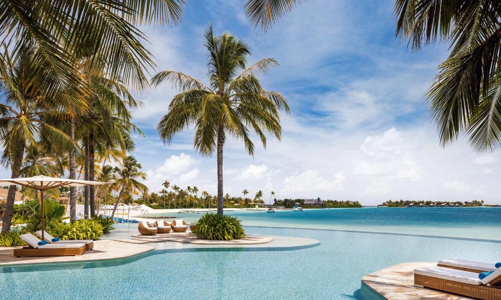 an infinity pool with palm trees and chairs at Waldorf Astoria Maldives Ithaafushi in South Male Atoll