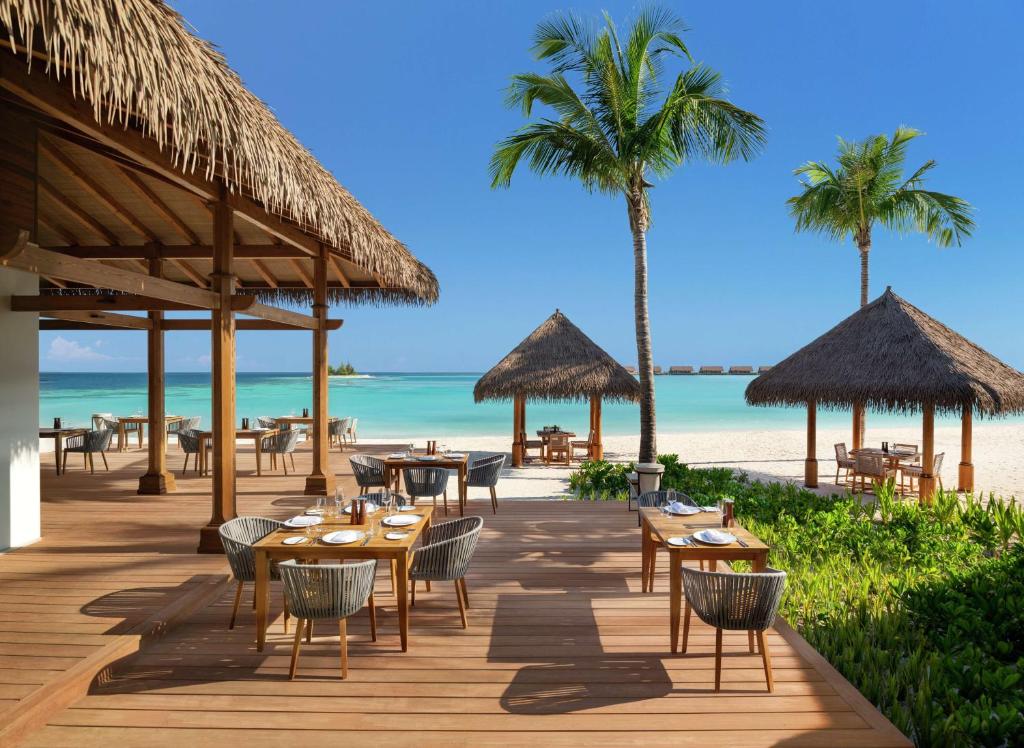 a restaurant on the beach with tables and chairs at Waldorf Astoria Maldives Ithaafushi in South Male Atoll