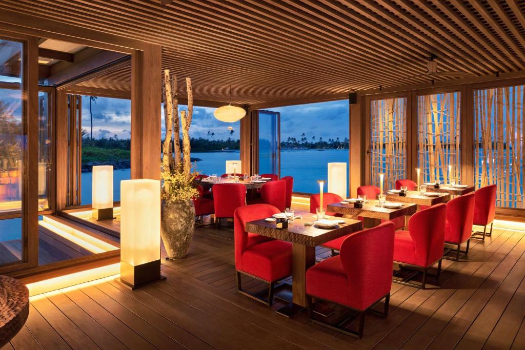a dining room with red chairs and tables and windows at Waldorf Astoria Maldives Ithaafushi in South Male Atoll