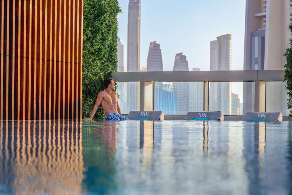 ドバイにあるWaldorf Astoria Dubai International Financial Centreの都会のスイミングプールに座る男