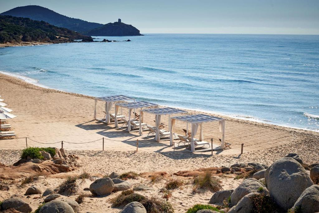 a beach with a row of umbrellas and the ocean at Conrad Chia Laguna Sardinia in Chia