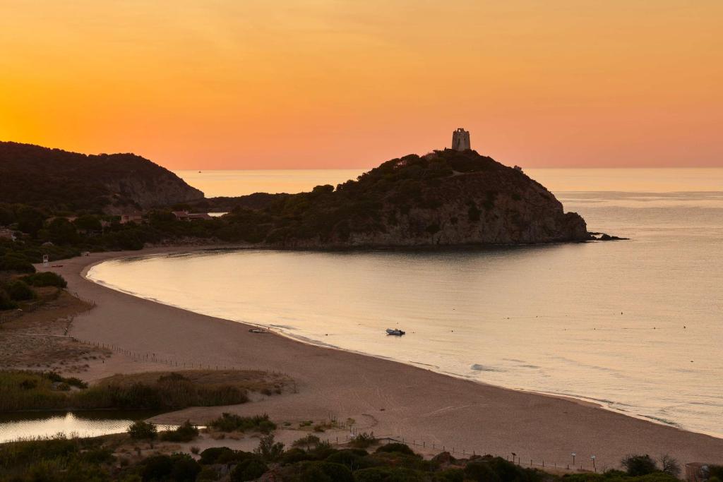 a lighthouse on an island in the ocean at sunset at Conrad Chia Laguna Sardinia in Chia