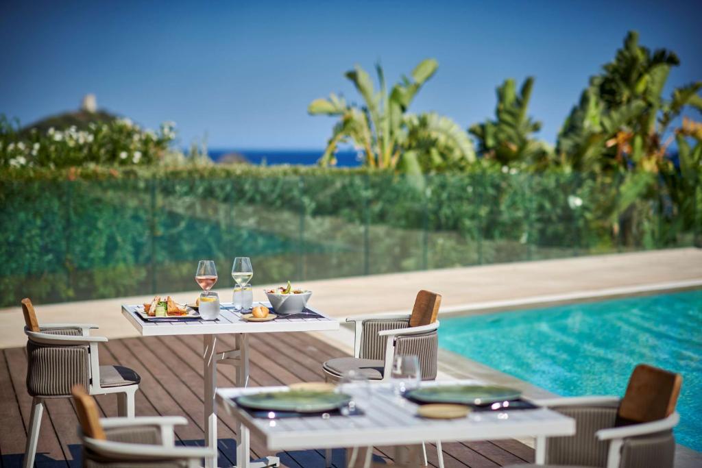 a table and chairs with wine glasses next to a pool at Conrad Chia Laguna Sardinia in Chia