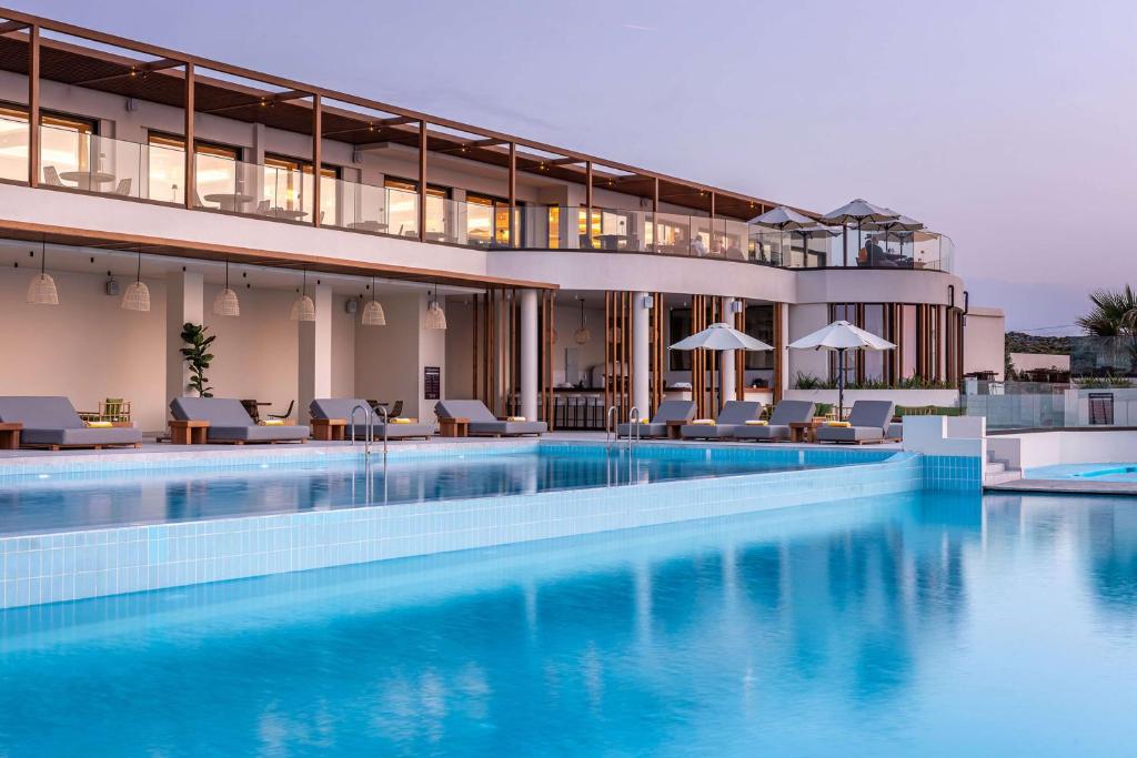 a large swimming pool with chairs and a building at Isla Brown Chania Resort, Curio Collection by Hilton in Stavros