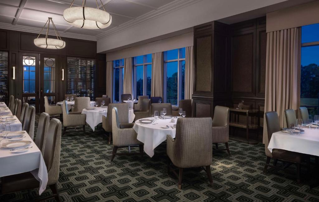 a restaurant with white tables and chairs and windows at Waldorf Astoria Orlando - An Official Walt Disney World Hotel in Orlando