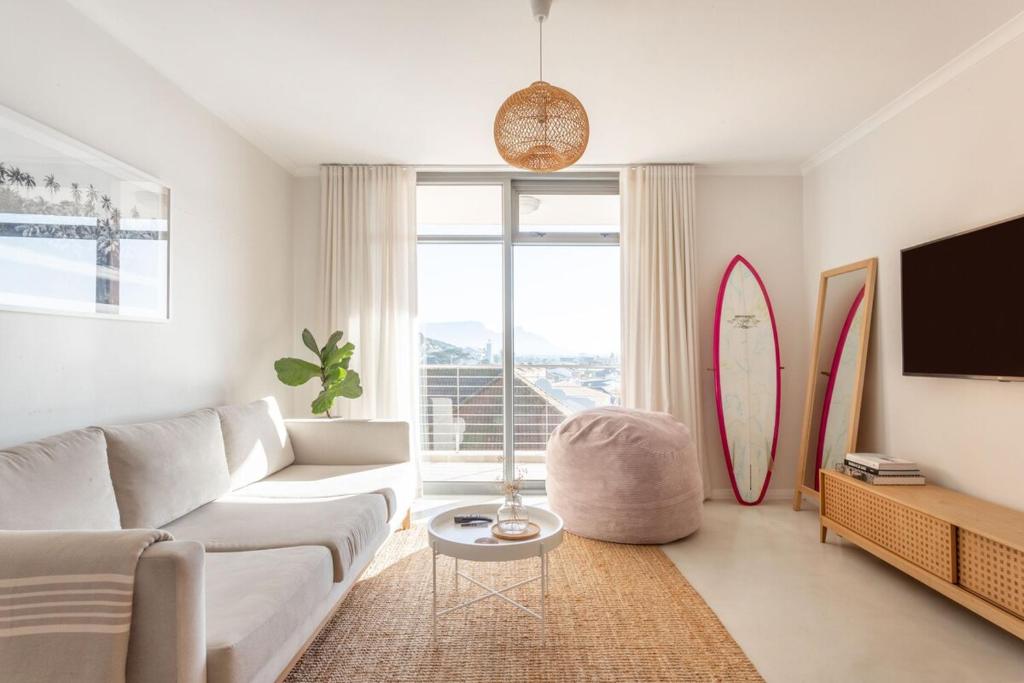a living room with a white couch and surfboards at 1 Bedroom Muizenberg Beach Apartment with Pool and Mountain Views in Muizenberg