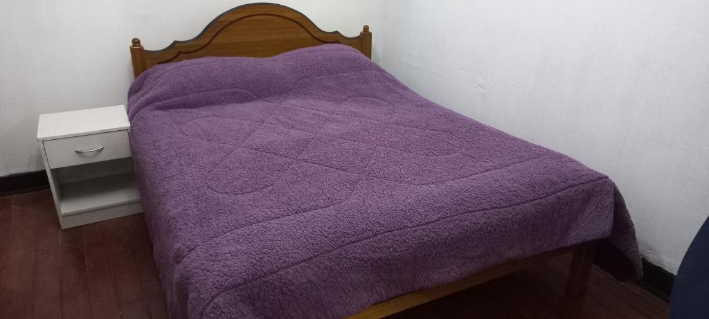 Una cama con una manta morada encima. en Alojamiento Yanira, en Valparaíso