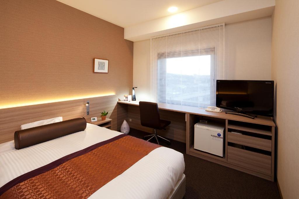 a hotel room with a bed and a desk with a television at Ueda Tokyu REI Hotel in Ueda