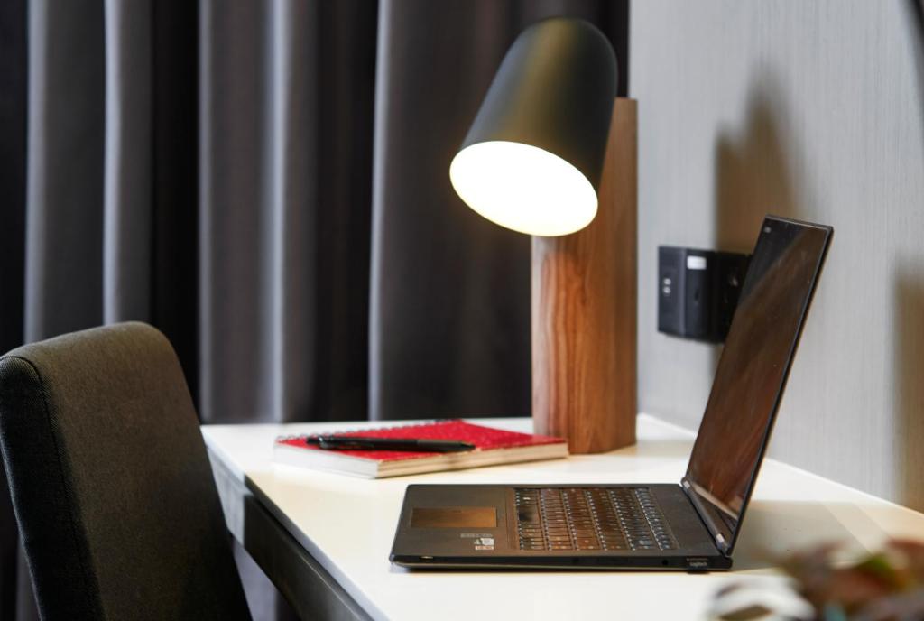 A compact hotel desk is set up with a laptop, task lamp, and writing materials.